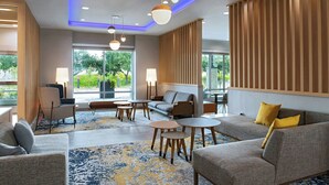 Un moderno vestíbulo de hotel con sofá, sillones, mesas y un gran ventanal que ofrece vistas a zonas verdes.