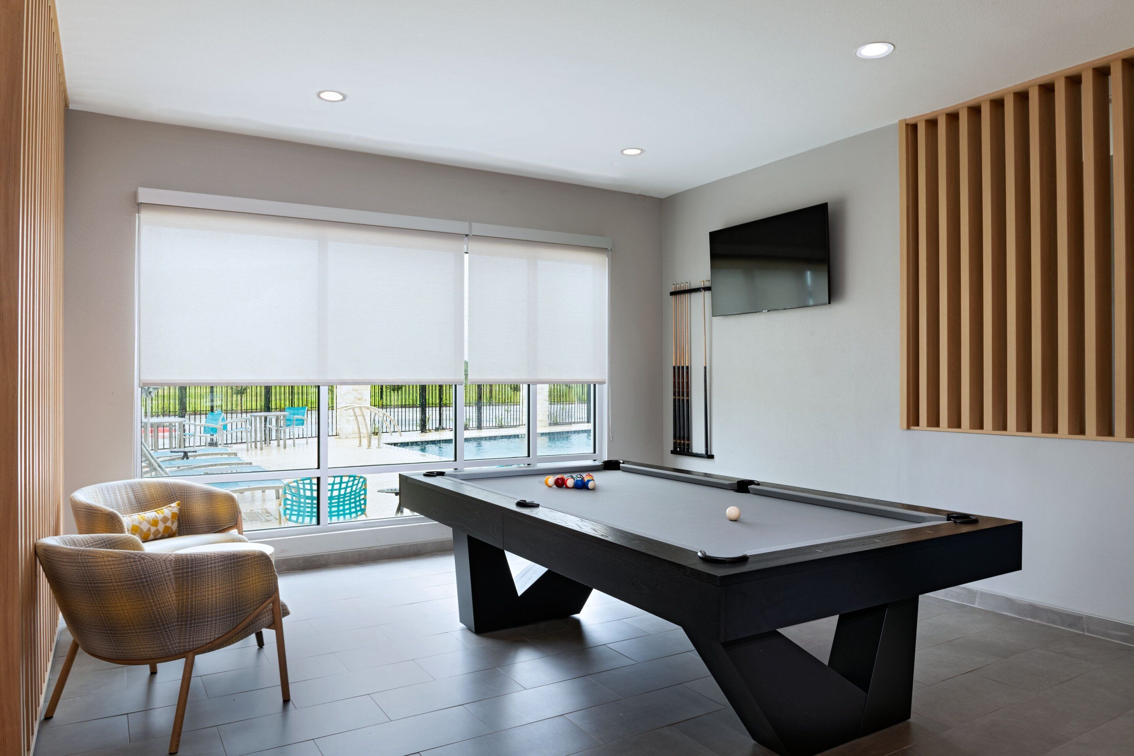 A modern room with a pool table, comfortable seating, and a large window offering a view of the outdoors.