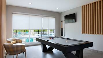 A modern room with a pool table, comfortable seating, and a large window offering a view of the outdoors.
