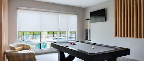 Una habitación moderna con mesa de billar, asientos cómodos y un amplio ventanal con vistas al exterior.