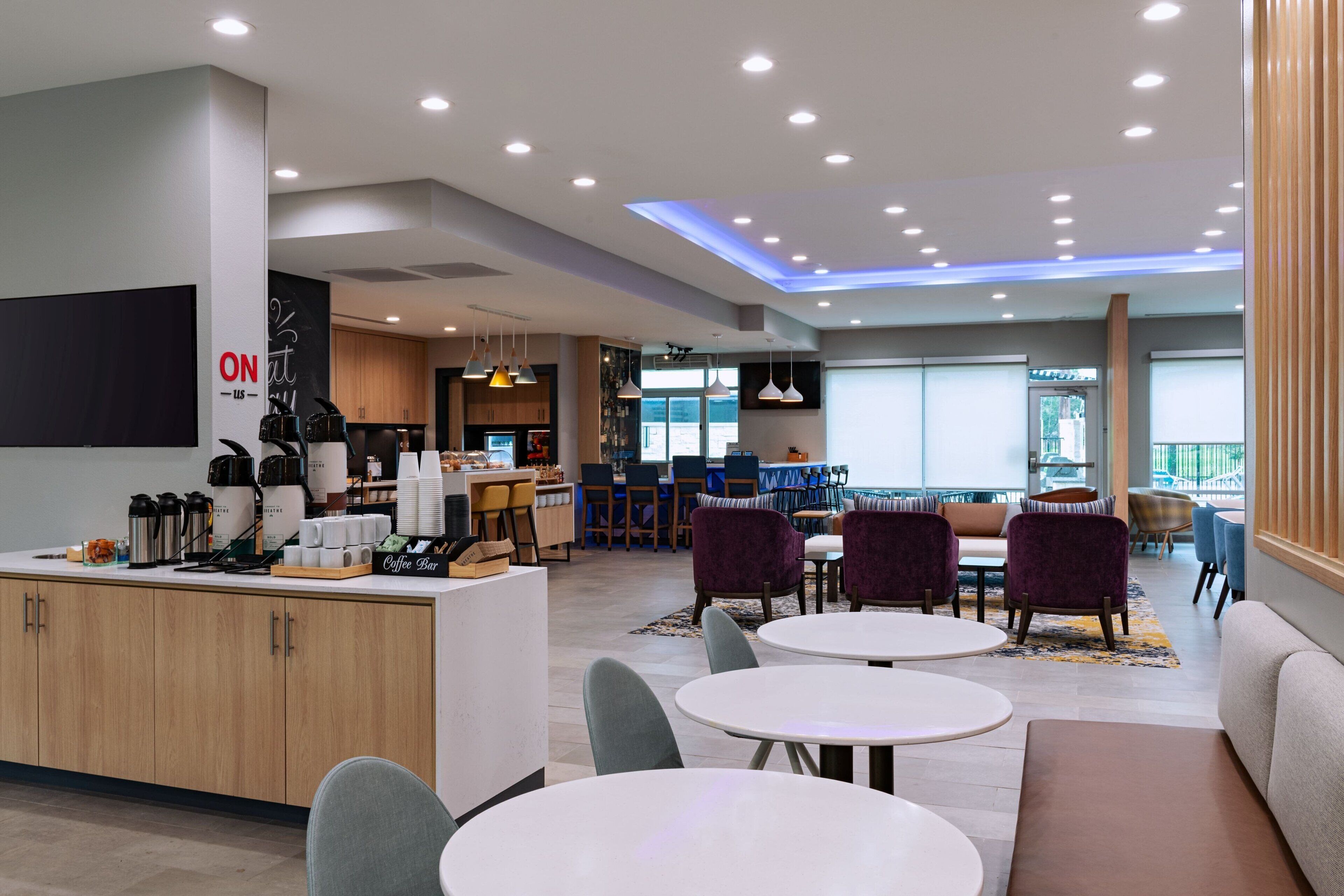 A modern hotel lobby with a coffee bar, seating area, and a view of the outdoors.