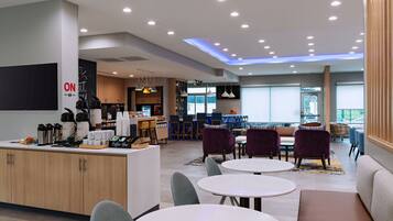 A modern hotel lobby with a coffee bar, seating area, and a view of the outdoors.