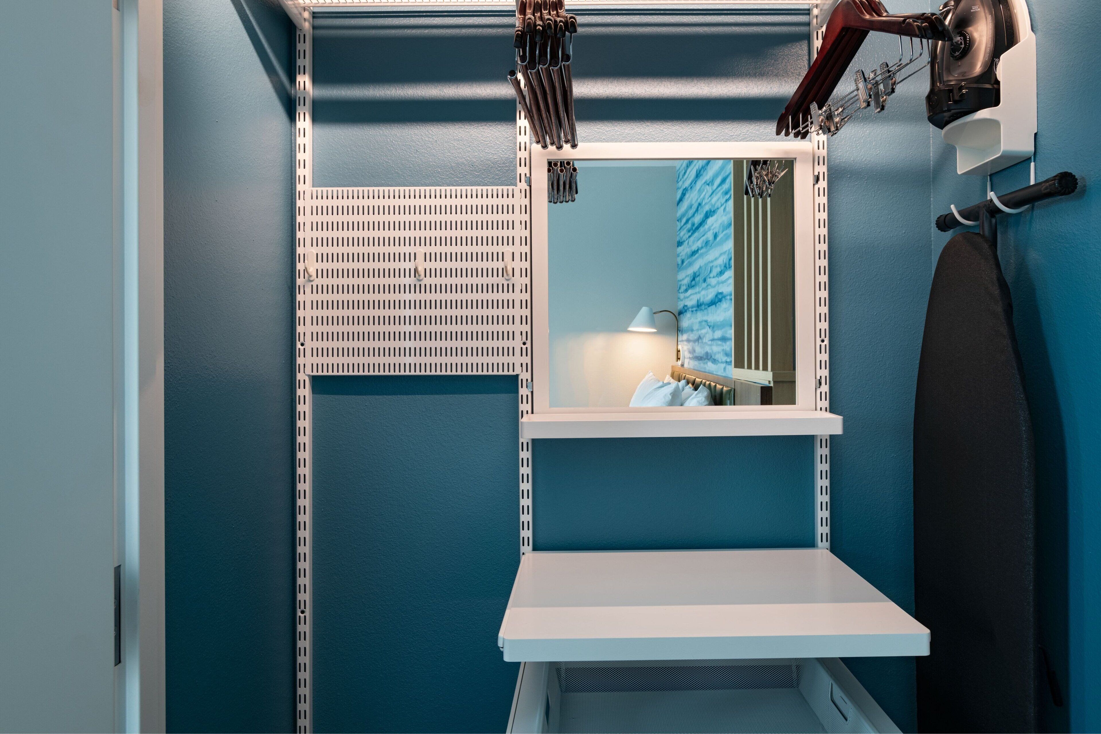 Un baño con pared azul, estante blanco, espejo y toallero.