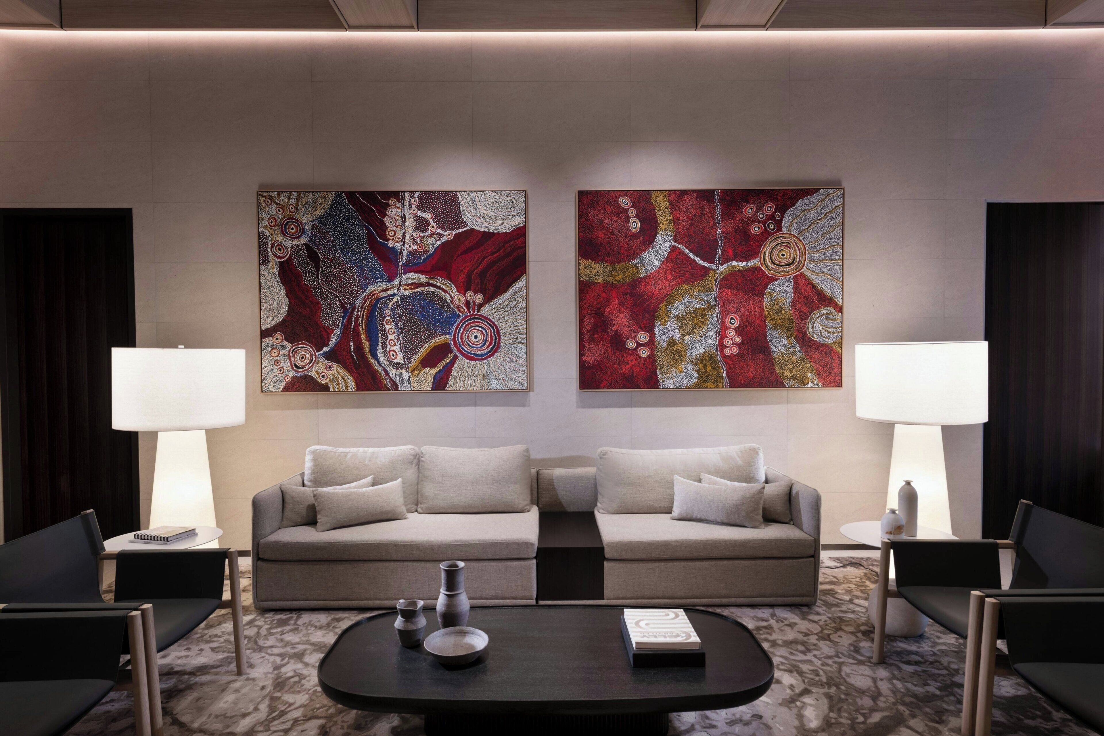 Un salon moderne comprenant un ensemble de canapés, deux tables d’appoint avec des lampes, une table basse et des tableaux abstraits accrochés au mur.
