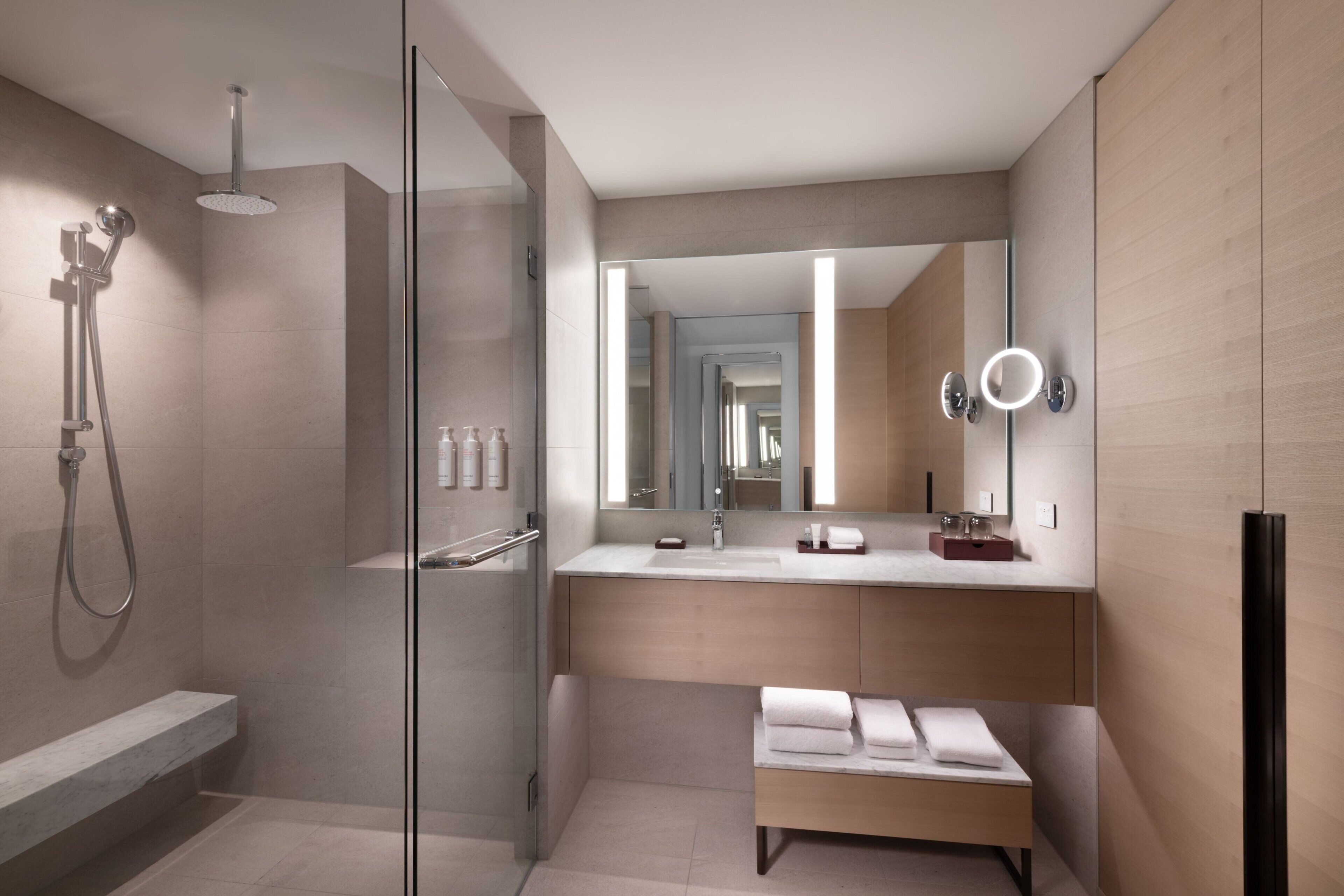 Une salle de bain moderne avec une douche à parois de verre, un meuble-lavabo doté d’un grand miroir et un banc avec des serviettes.