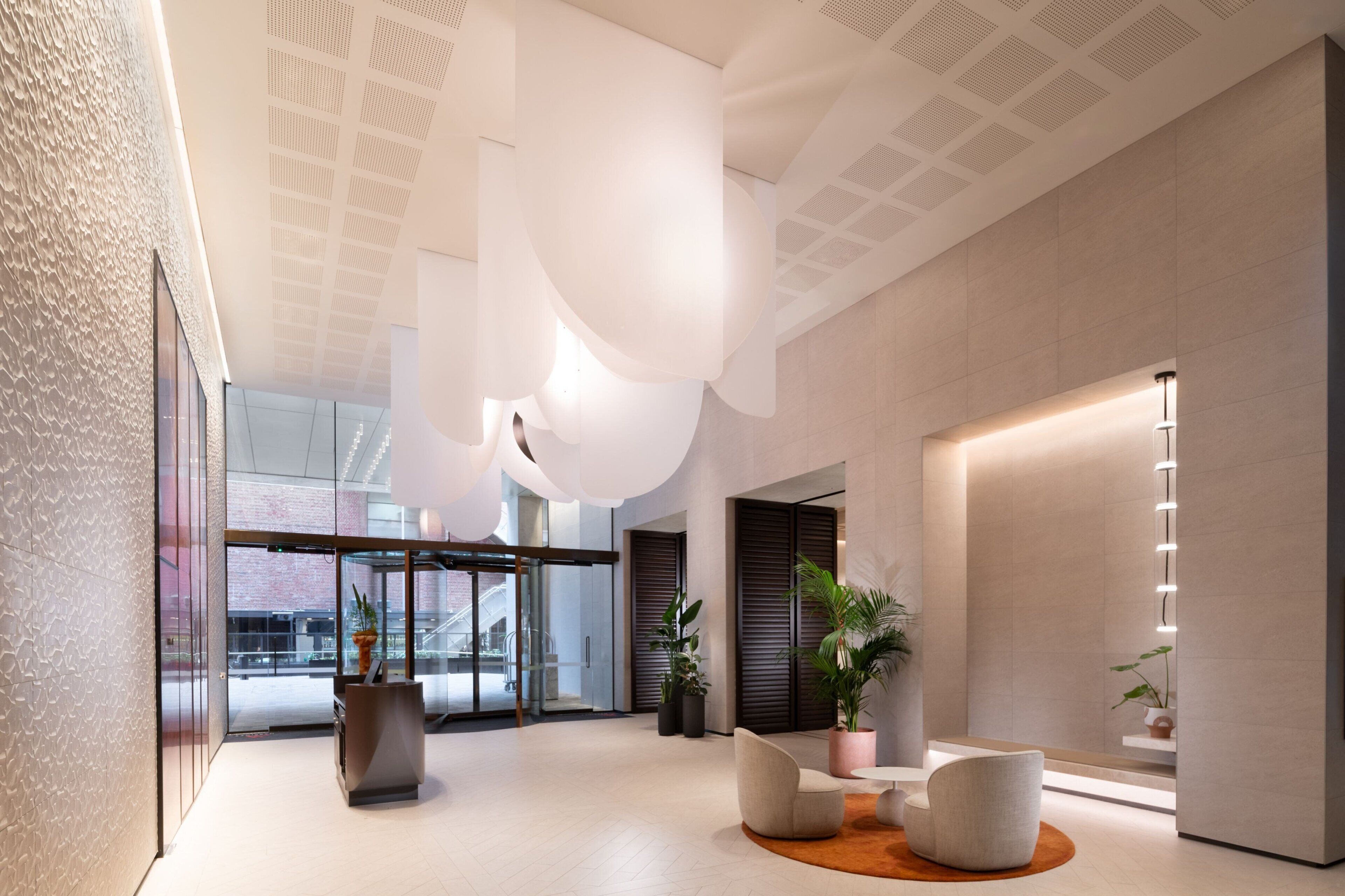 Eine moderne Lobby mit Glastür, einer Rezeption, einer Sitzecke und einer großen Pflanze.