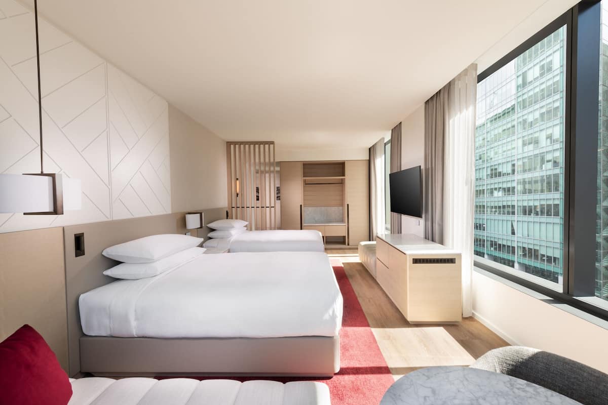 Moderni hotellihuone, jossa on kaksi sänkyä, televisio ja suuri ikkuna, josta avautuu näkymä kaupunkiin.