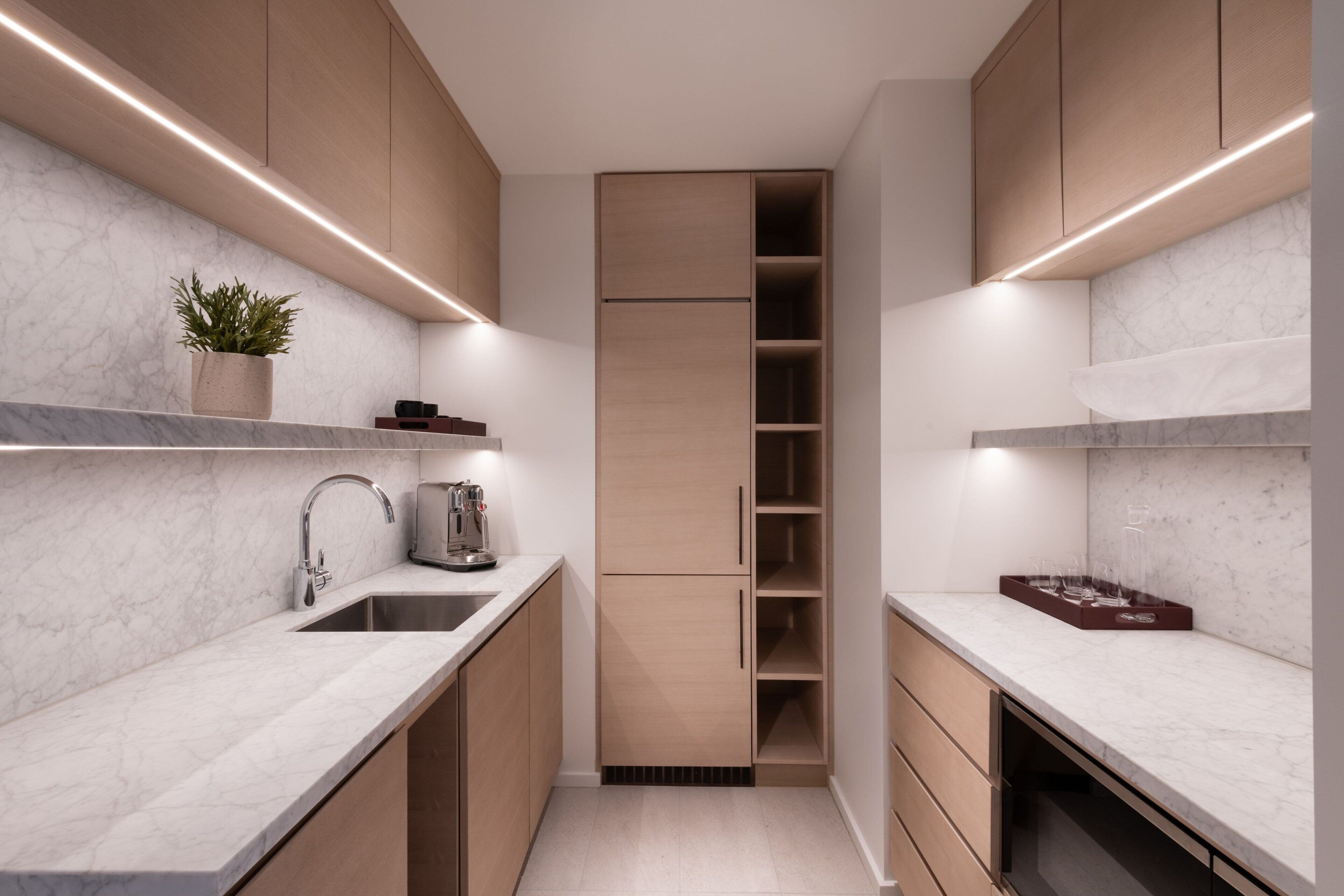 A modern kitchen with marble countertops, wooden cabinets, and built-in shelving.