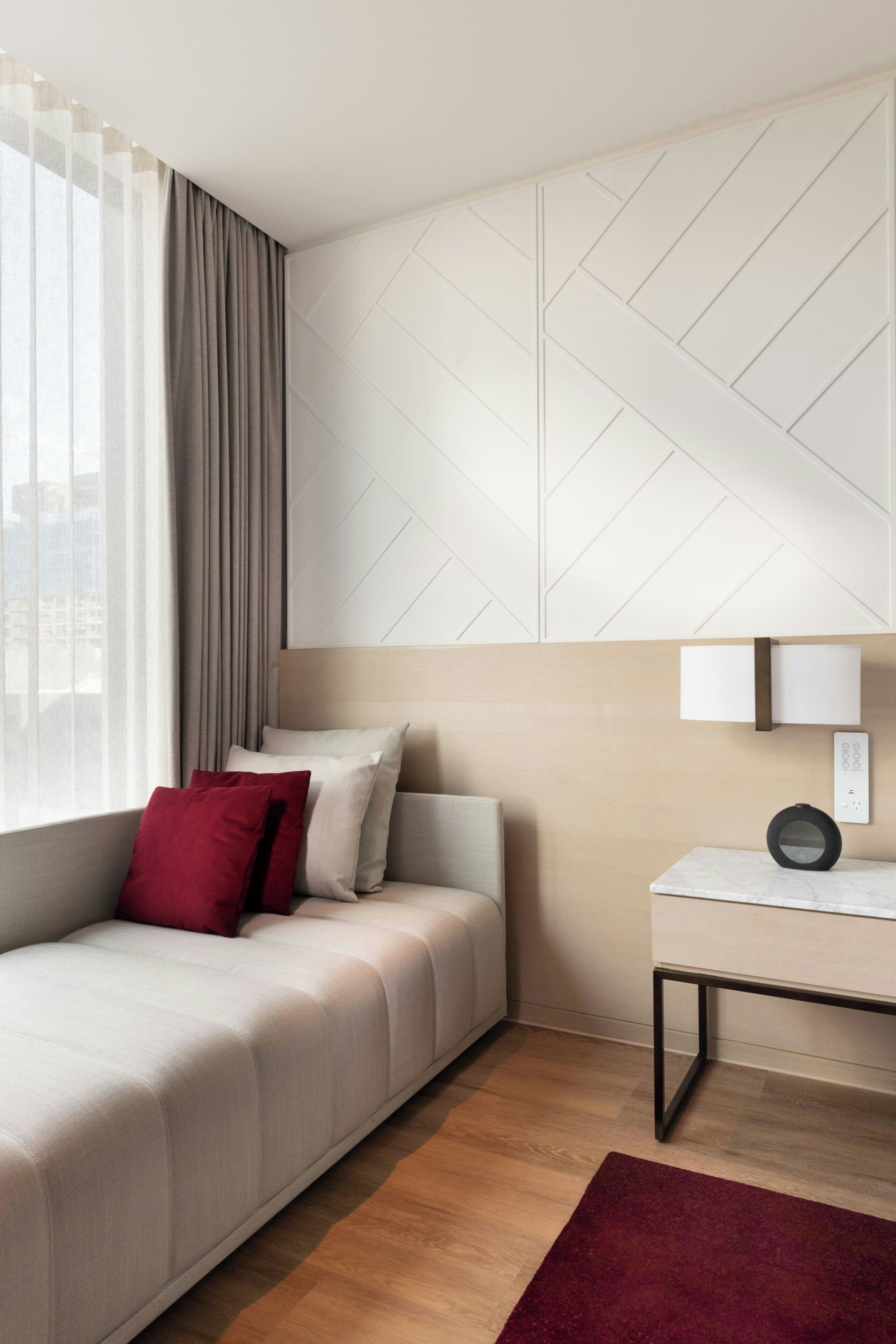 A modern hotel room with a sofa, a bedside table, and a lamp.