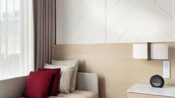 A modern hotel room with a sofa, a bedside table, and a lamp.