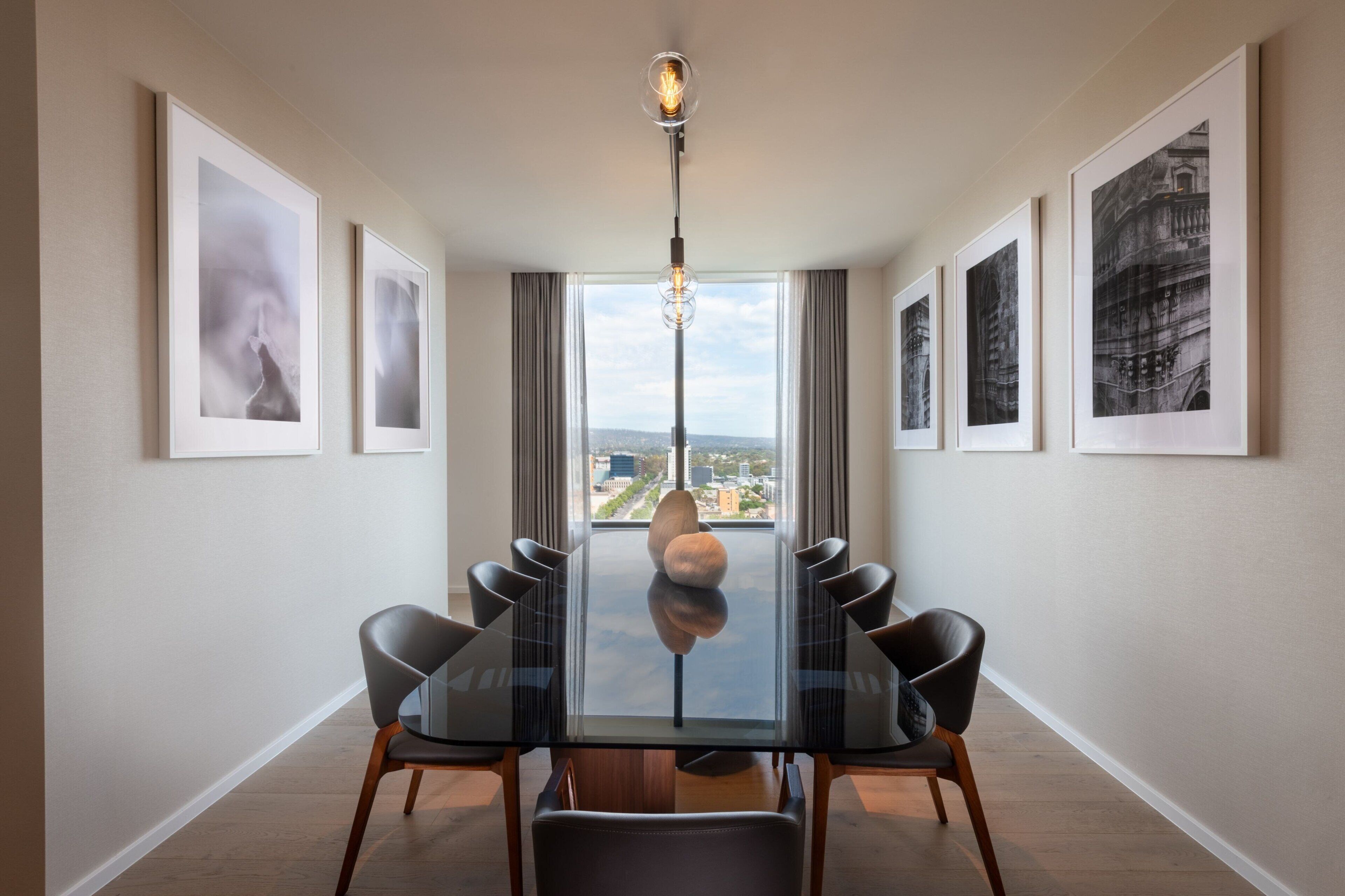 A modern dining room with a glass table, black chairs, and framed artwork on the walls.
