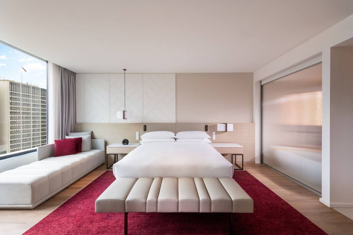 Moderni hotellihuone, jossa on suuri sänky, sohva, yöpöytä ja näkymä kaupunkiin.