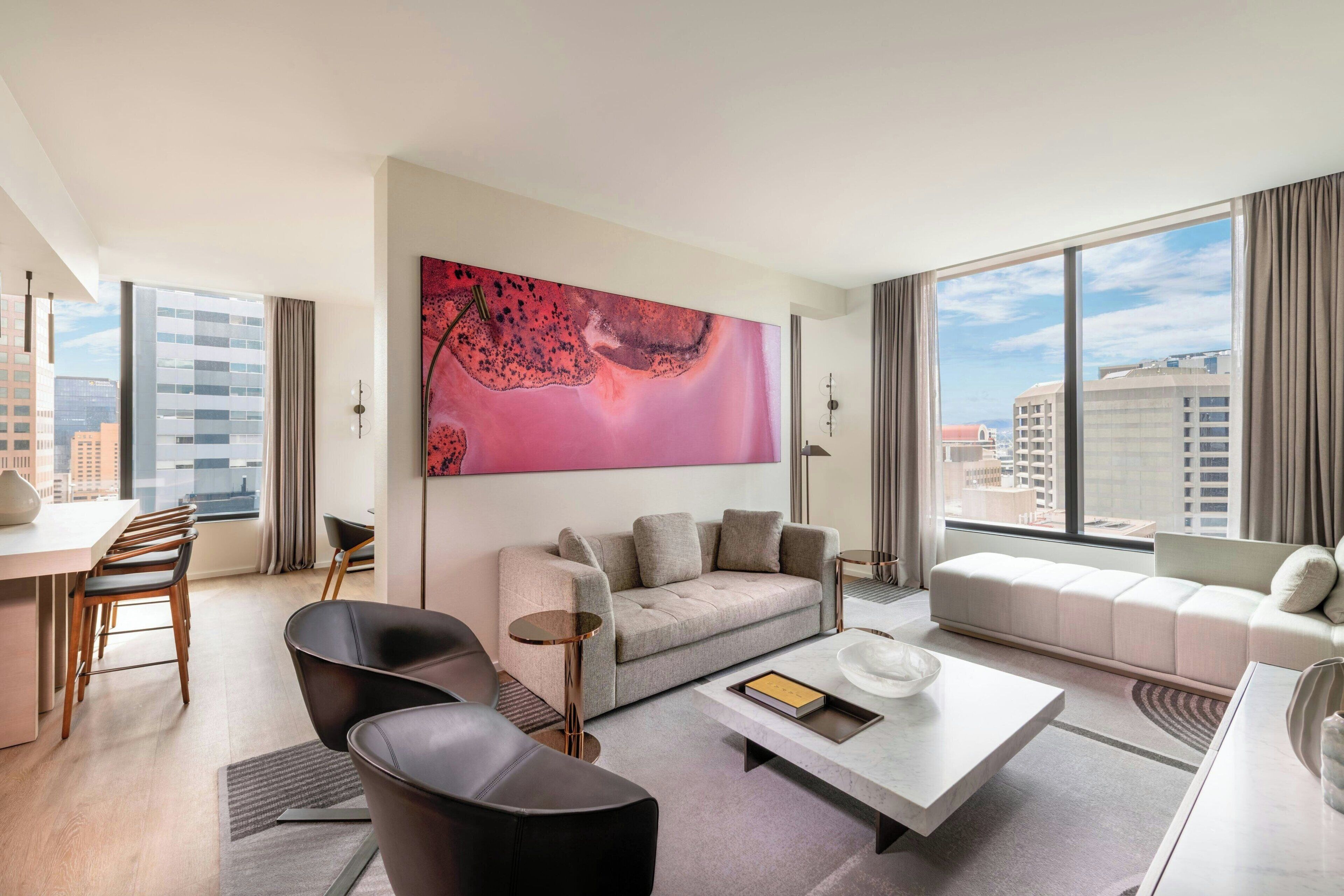 Ein modernes Hotelzimmer mit großem Fenster, einer Couch, einem Couchtisch und einem Essbereich mit Stühlen.