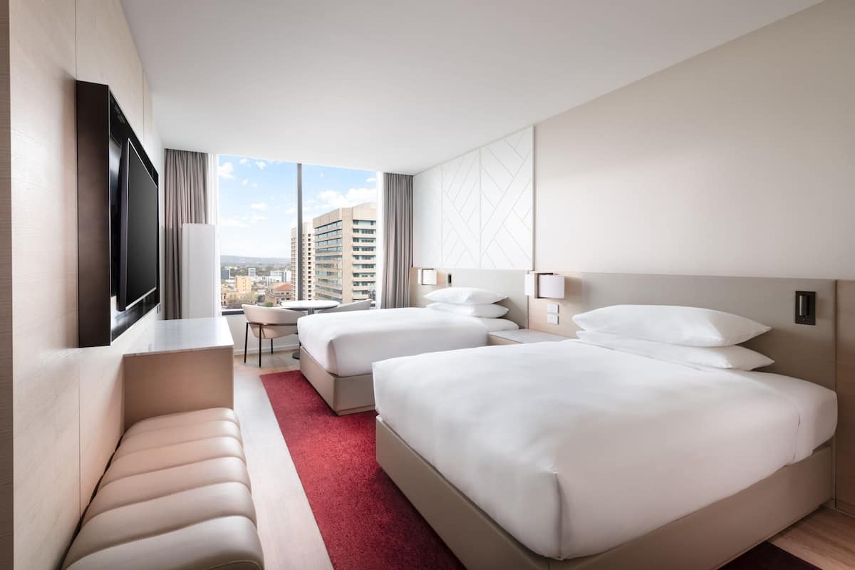 Hotellihuone, jossa on kaksi sänkyä, työpöytä, televisio ja näkymä kaupunkiin.