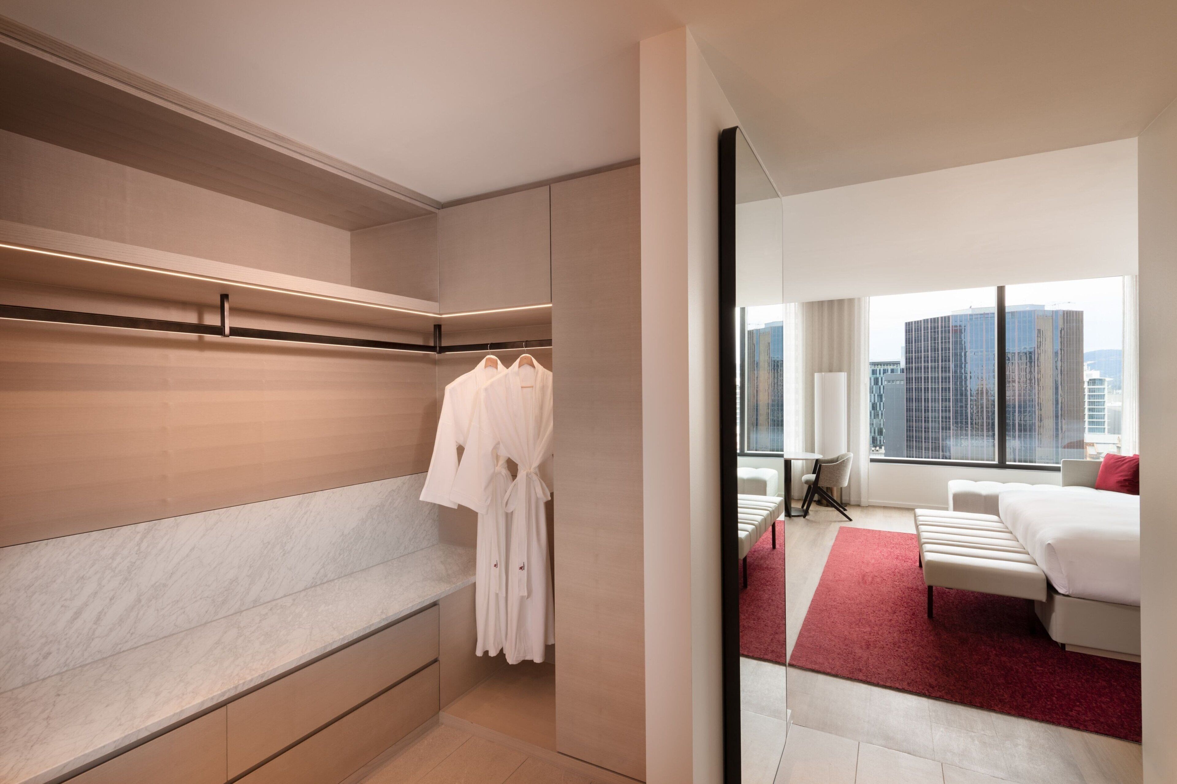 A modern hotel room with a large bed, a seating area, and a view of the cityscape.