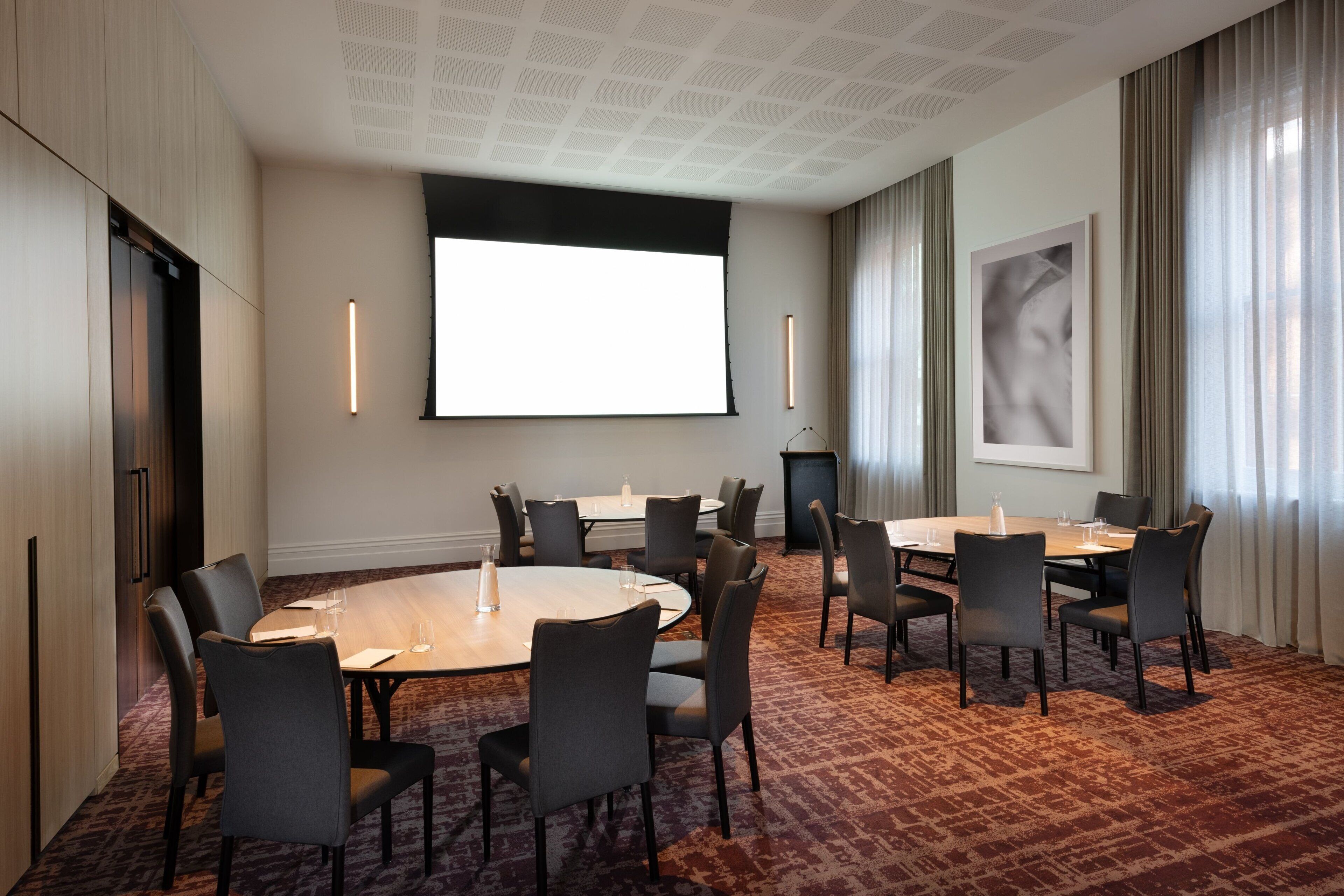 Un salón de conferencias con una pantalla grande, varias mesas y sillas.