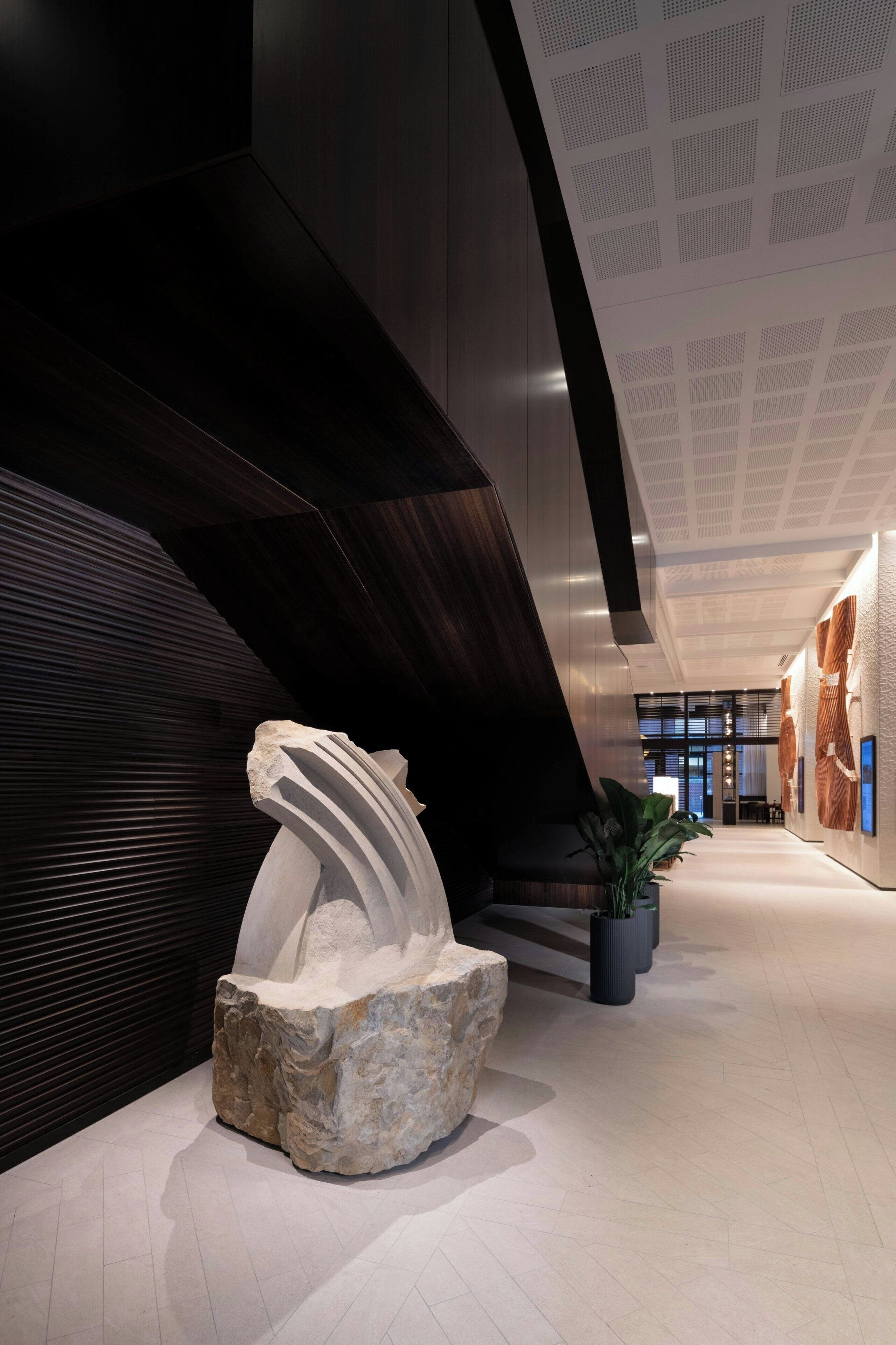 Um lobby moderno com uma grande escultura abstrata, painéis de madeira escura e teto padronizado.