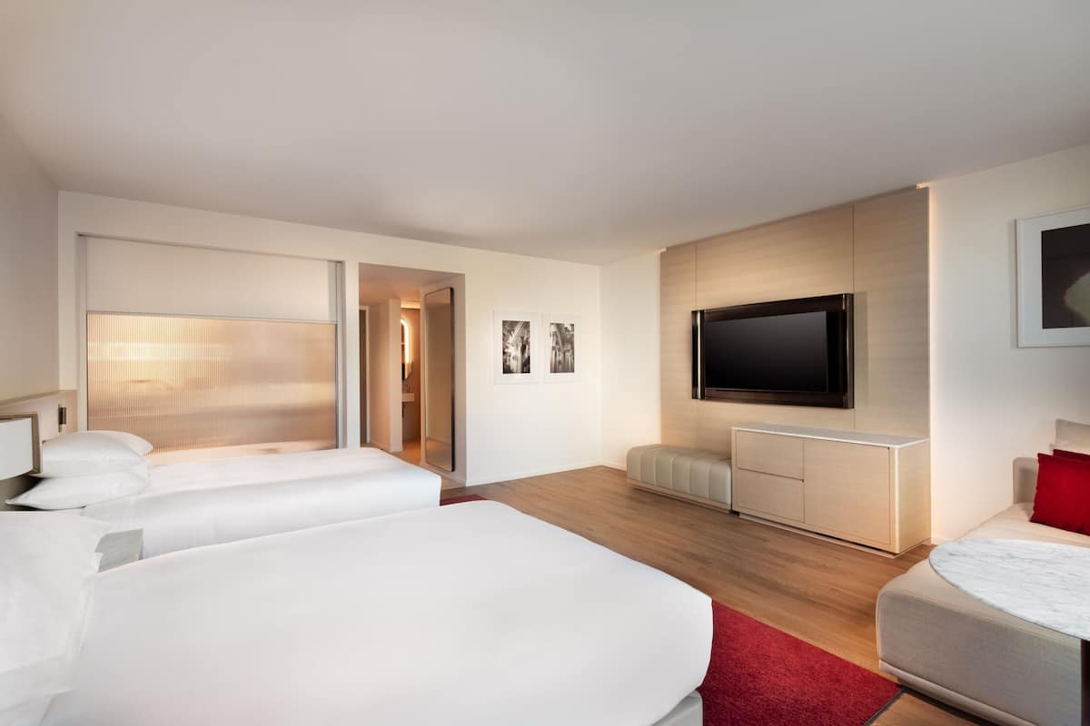 Moderni hotellihuone, jossa on kaksi sänkyä, televisio ja punainen tehosteseinä.