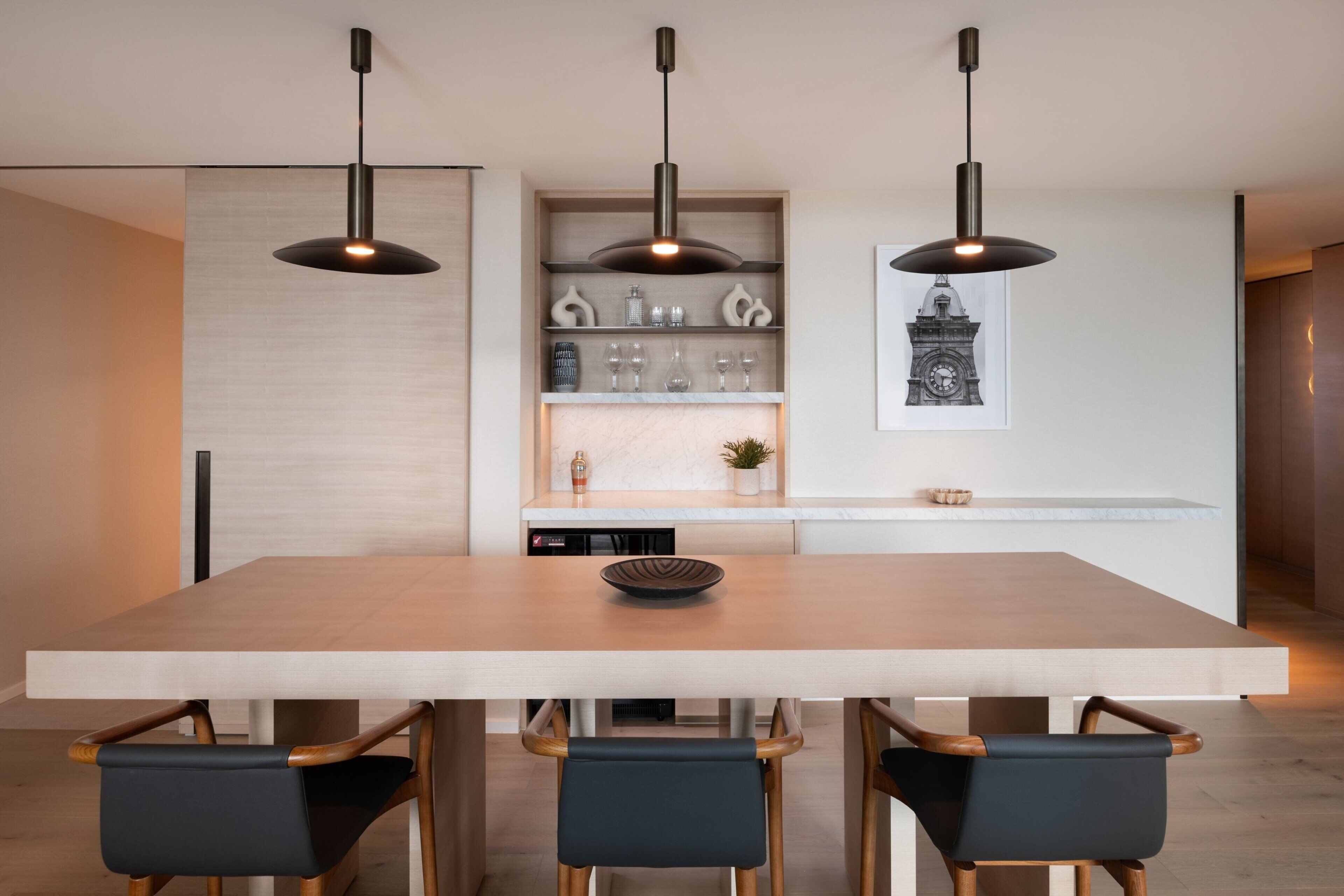 A modern kitchen with a large island, pendant lighting, and a dining area with a wooden table and chairs.