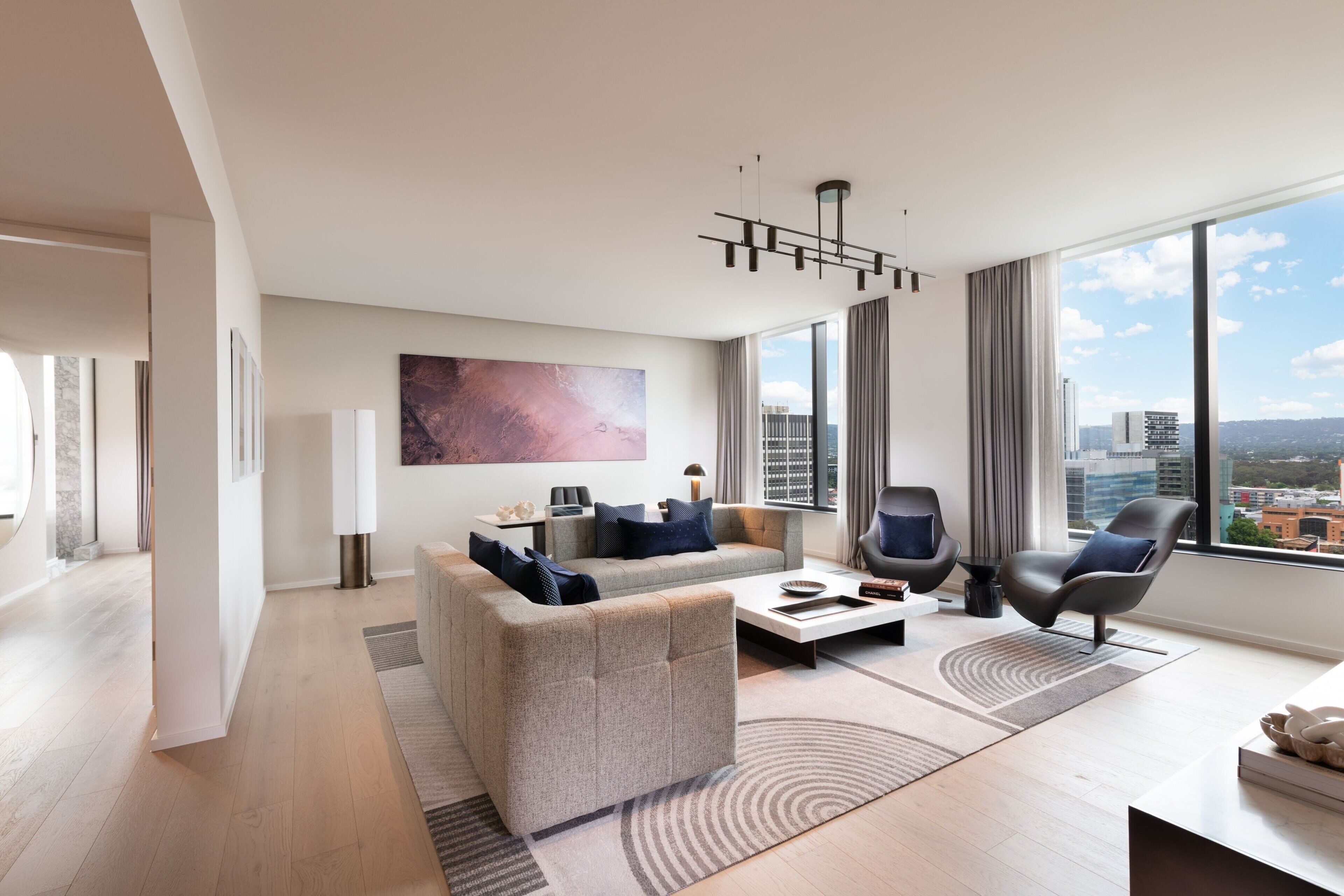 Una sala de estar moderna con un sofá, sillones y una mesa de centro. Hay un ventanal con vistas a la ciudad.