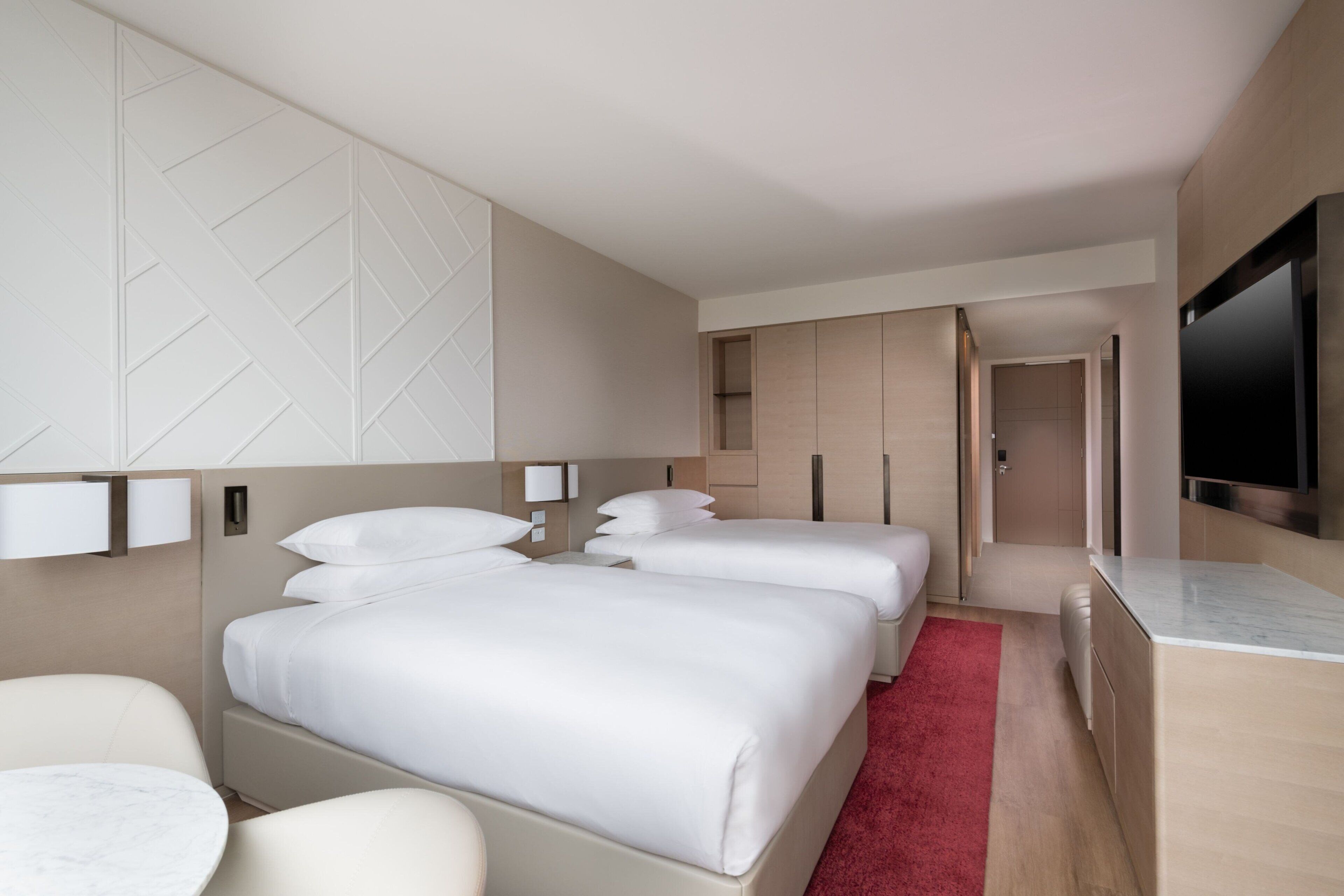 A modern hotel room with a large bed, a smaller bed, a desk, and a TV.