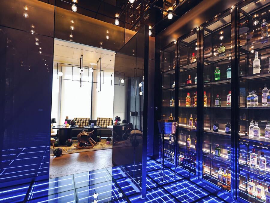 A modern bar area with a glass display case of liquor bottles, a seating area with a sofa and a coffee table, and a patterned floor.