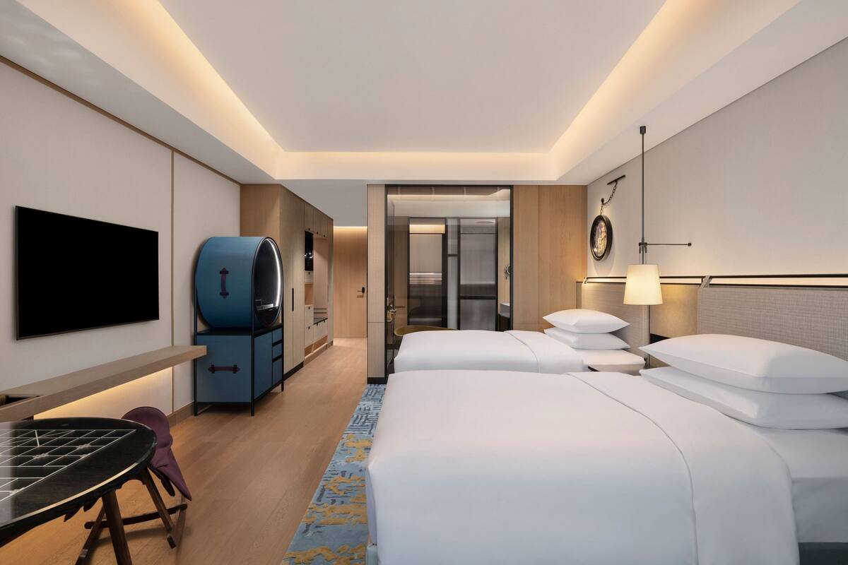 Une chambre d’hôtel équipée d’un lit, de tables de chevet, d’une télévision, d’un mini-bar et d’une salle de bain visible à travers une porte.
