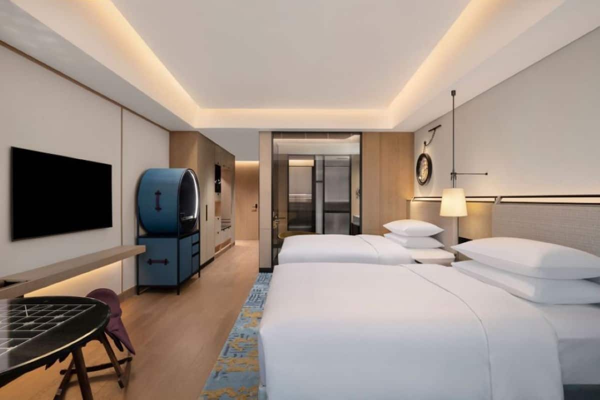 A hotel room with a bed, a desk, a TV, a minibar, and a bathroom door.