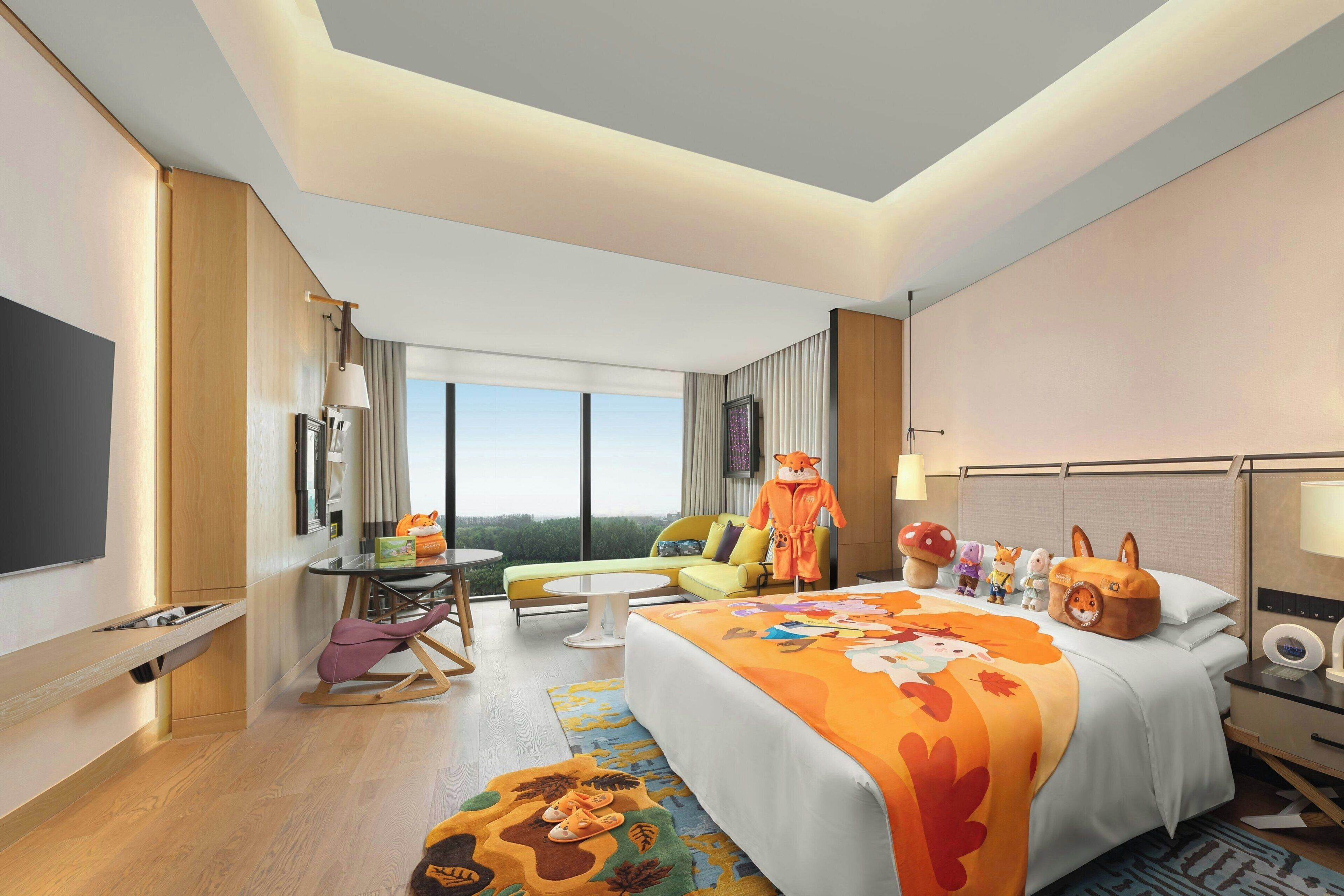 Quarto de hotel moderno com uma cama grande, um sofá, uma mesa de jantar, uma televisão e vista para o exterior.