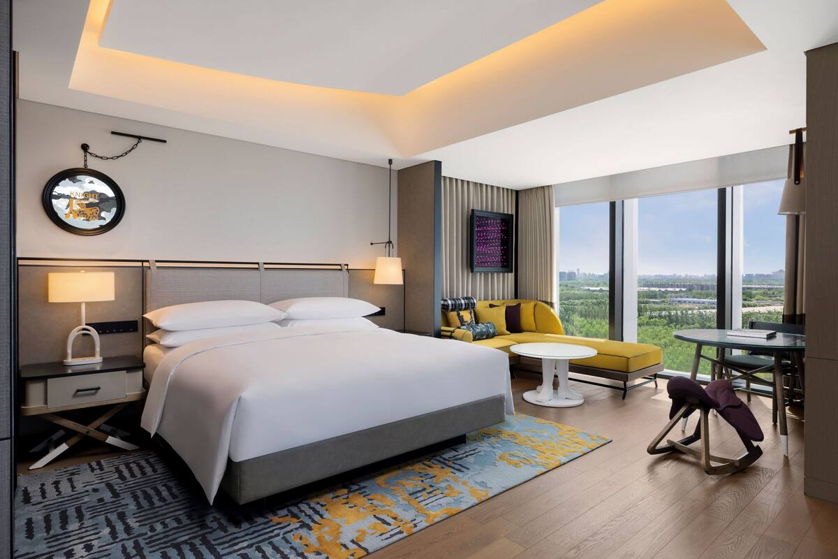 Une chambre d’hôtel moderne avec un grand lit, un canapé, une petite table et une vue sur la ville.
