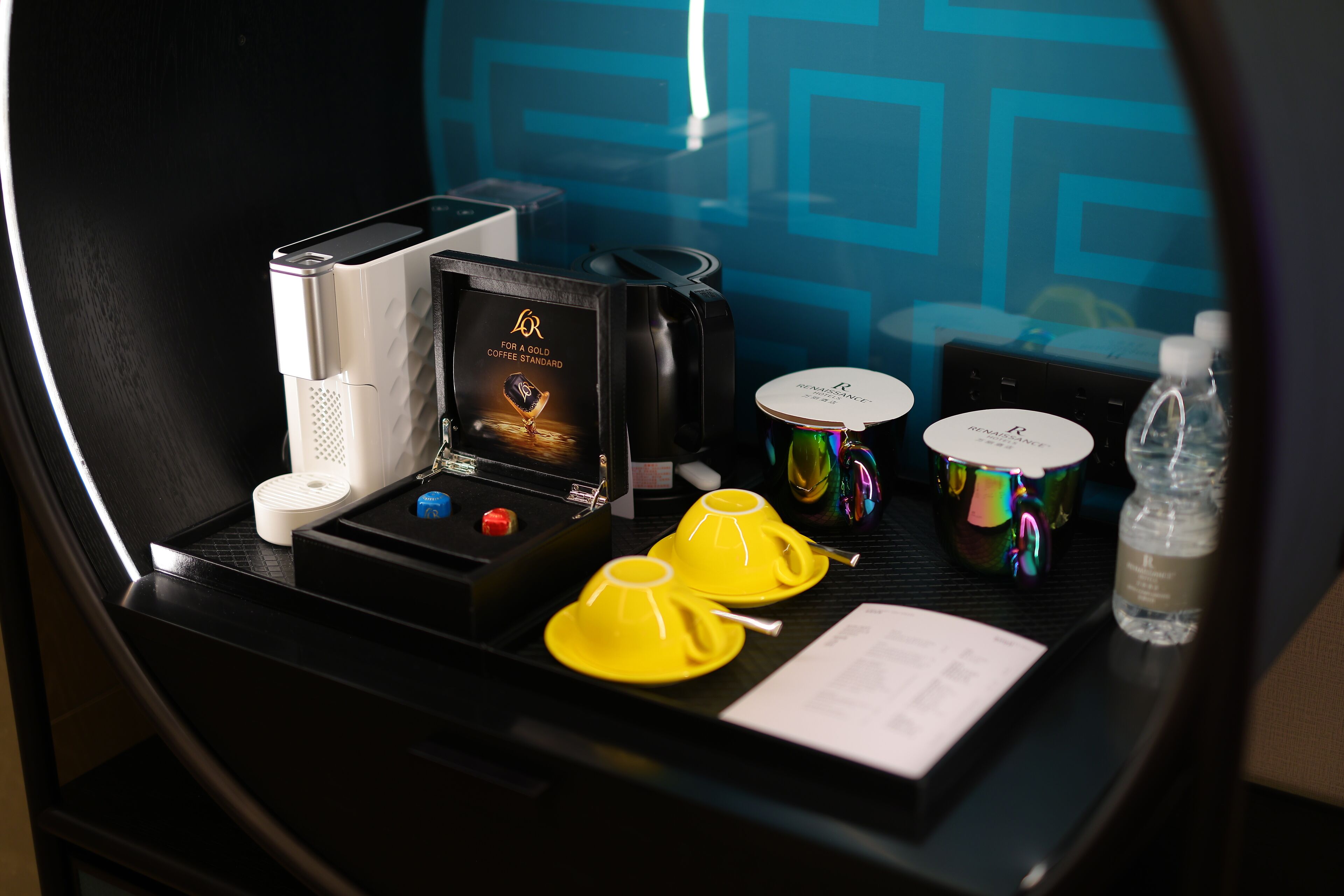 Minibar de una habitación de hotel, con una cafetera, un juego de té y una botella de agua.