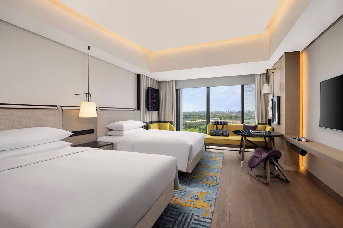A modern hotel room with two beds, a sofa, a small table, and a TV.