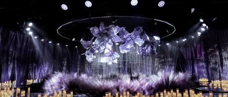 A stage with a central floral arrangement, multiple candles, and a dark backdrop.