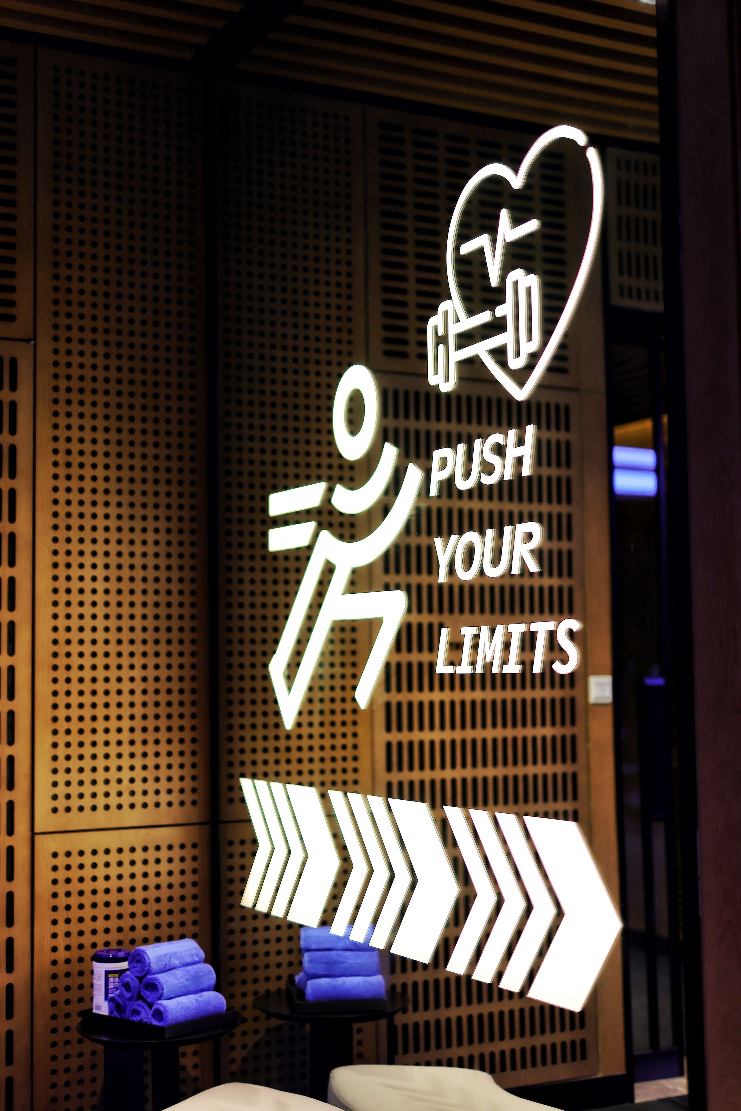 A motivational sign with a heart and a person lifting weights, surrounded by a room with a perforated wall and a massage table with towels.