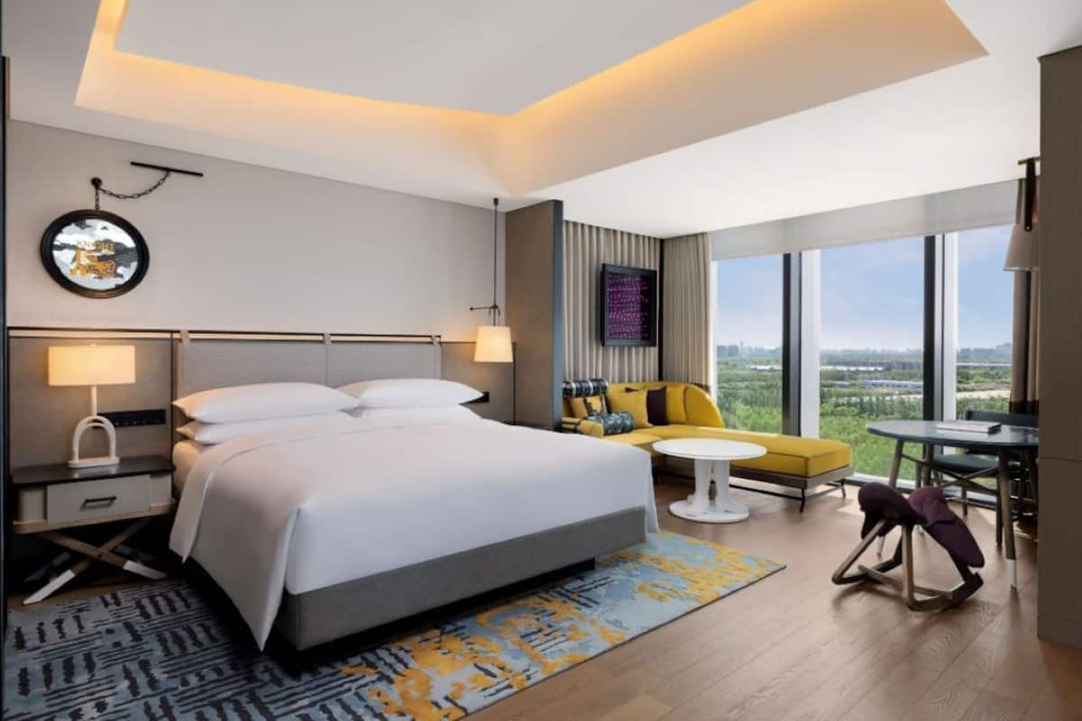 A modern hotel room with a large bed, a sofa, a small table, and a view of the city.