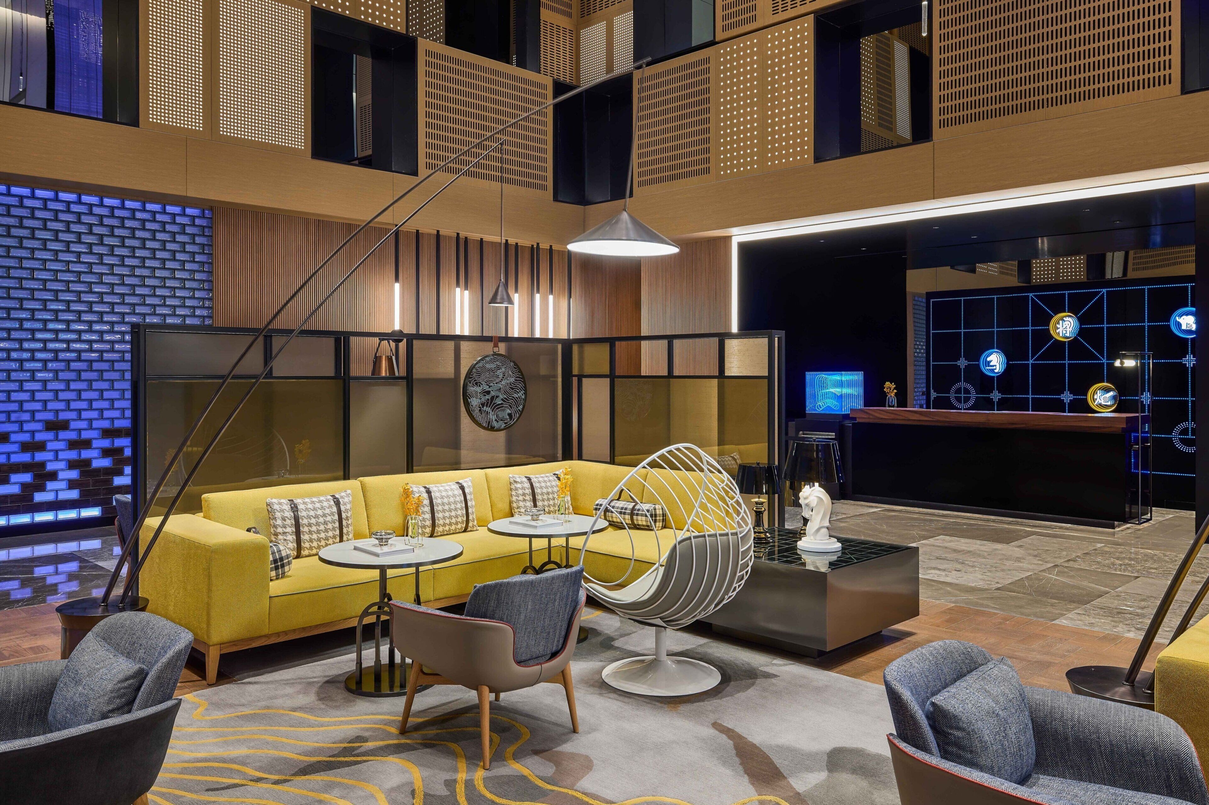Un hall d’entrée moderne avec un canapé jaune, des tables rondes et un fauteuil sphérique original.