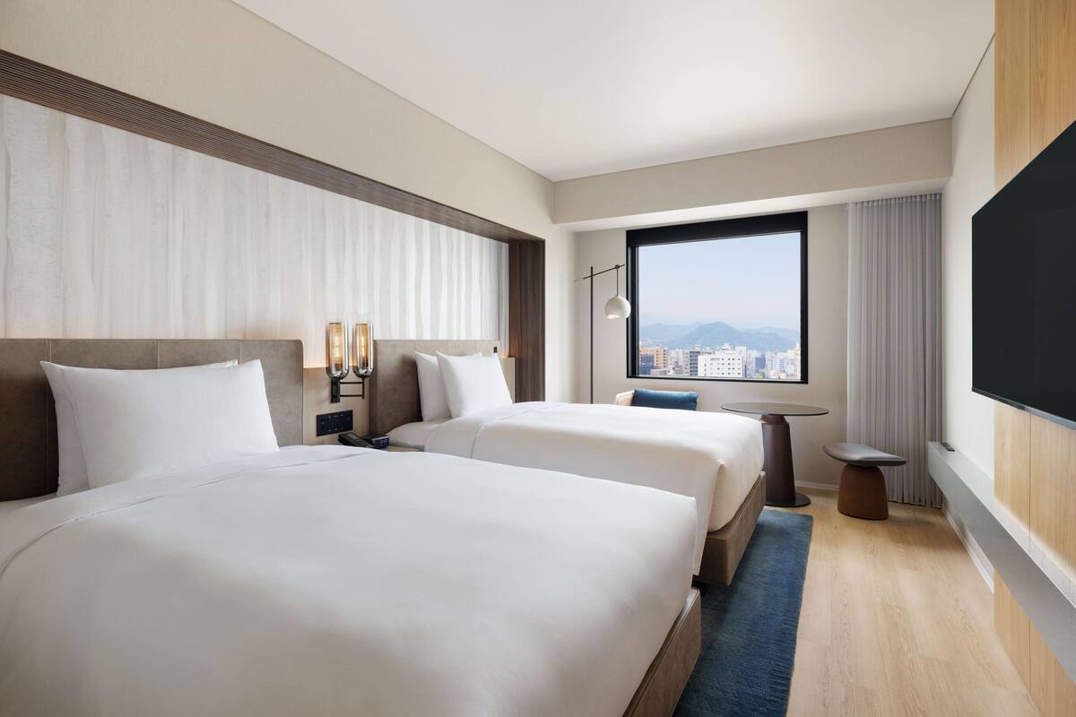 A hotel room with two beds, a city view, a flat-screen TV, and a small table.
