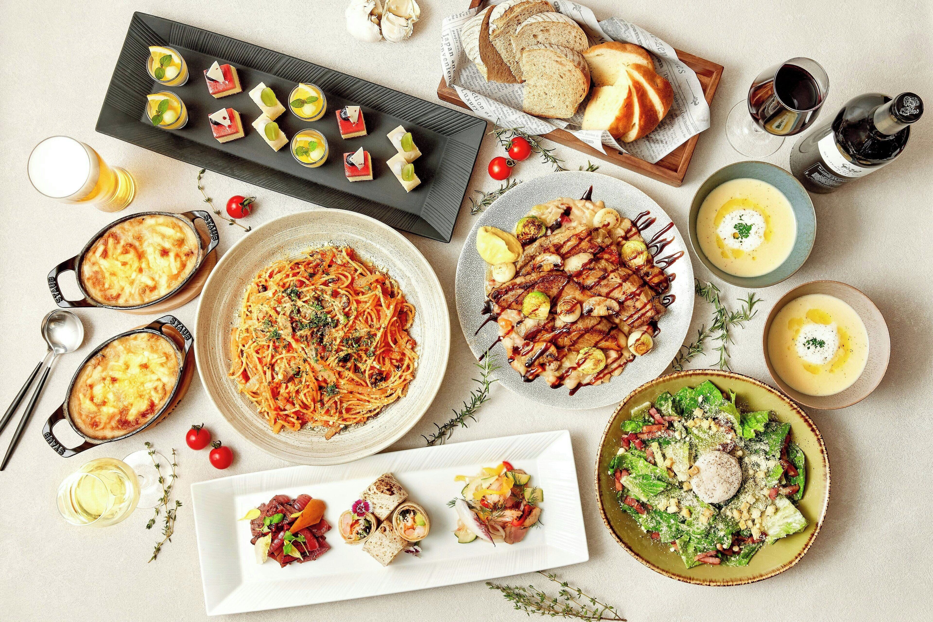A variety of dishes including pasta, grilled chicken, and salads, arranged on a table with bread and drinks.