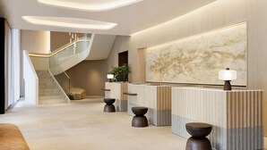 Un área de recepción moderna con una pared de mármol, una escalera y un mostrador de recepción con una lámpara.