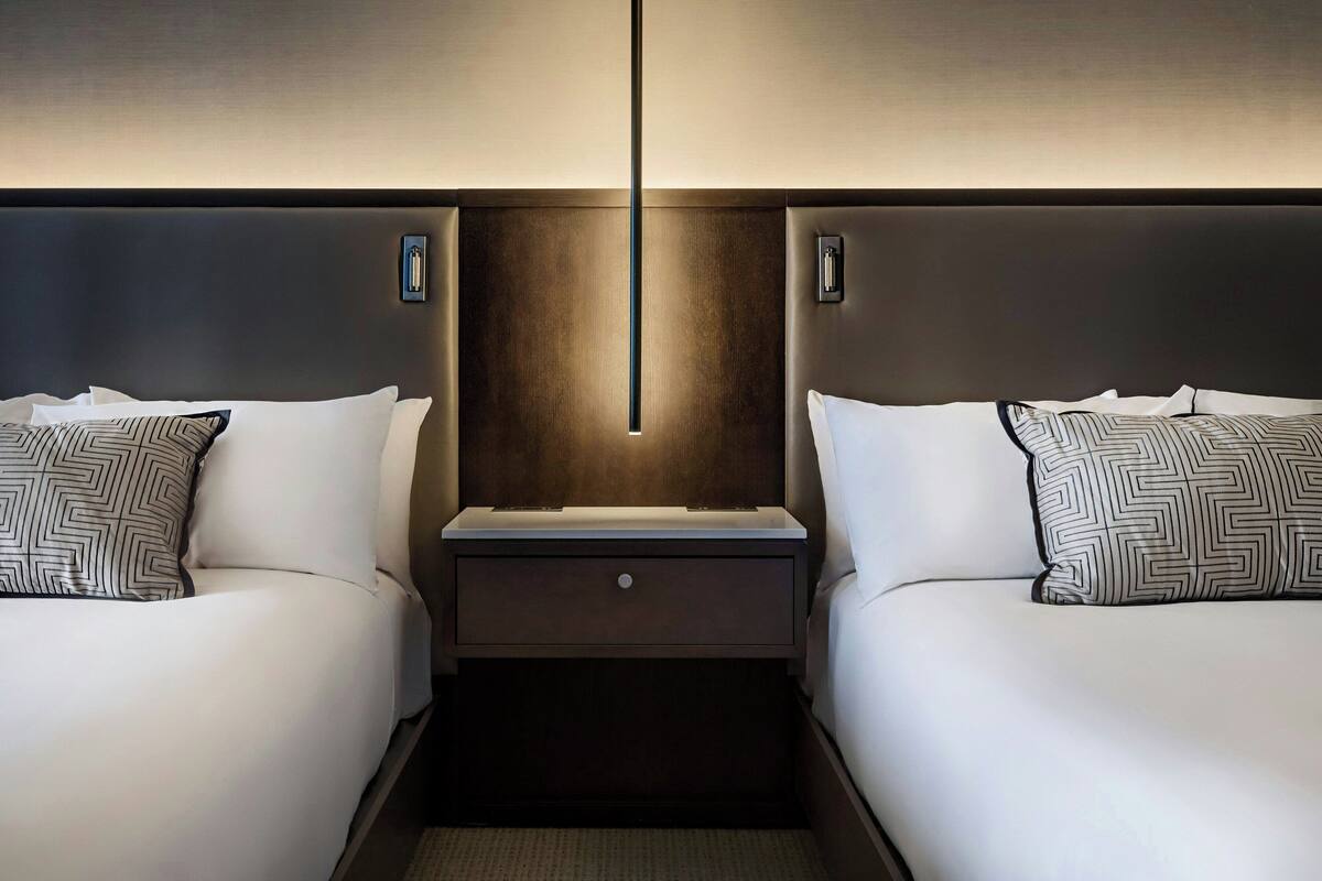 A hotel room with two beds, a nightstand, and a wall-mounted light fixture.