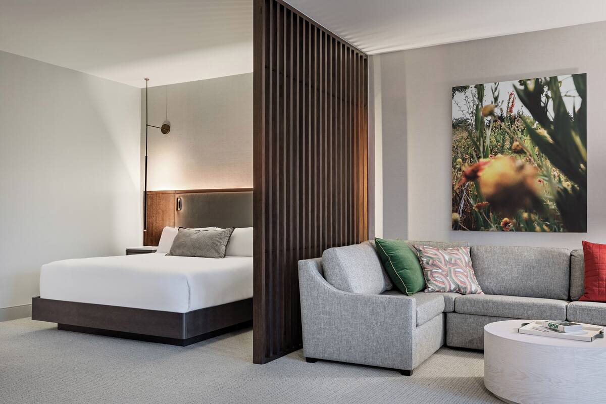 A modern hotel room with a bed, a sofa, a coffee table, and a large painting on the wall.