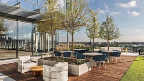 A rooftop patio with outdoor seating, large windows, and a view of the city. - HALL Park Hotel, Autograph Collection (Frisco)