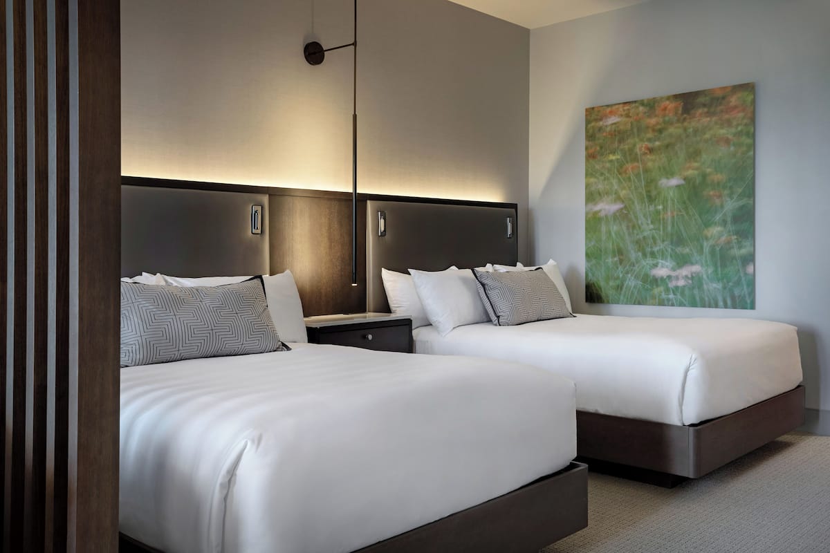 A hotel room with two beds, a large painting, and a modern headboard.