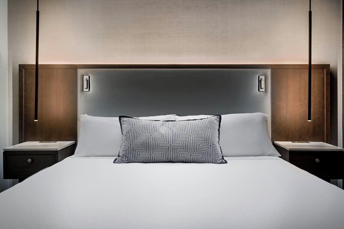 A modern hotel room with a large bed, two bedside tables, and a headboard with integrated lighting.