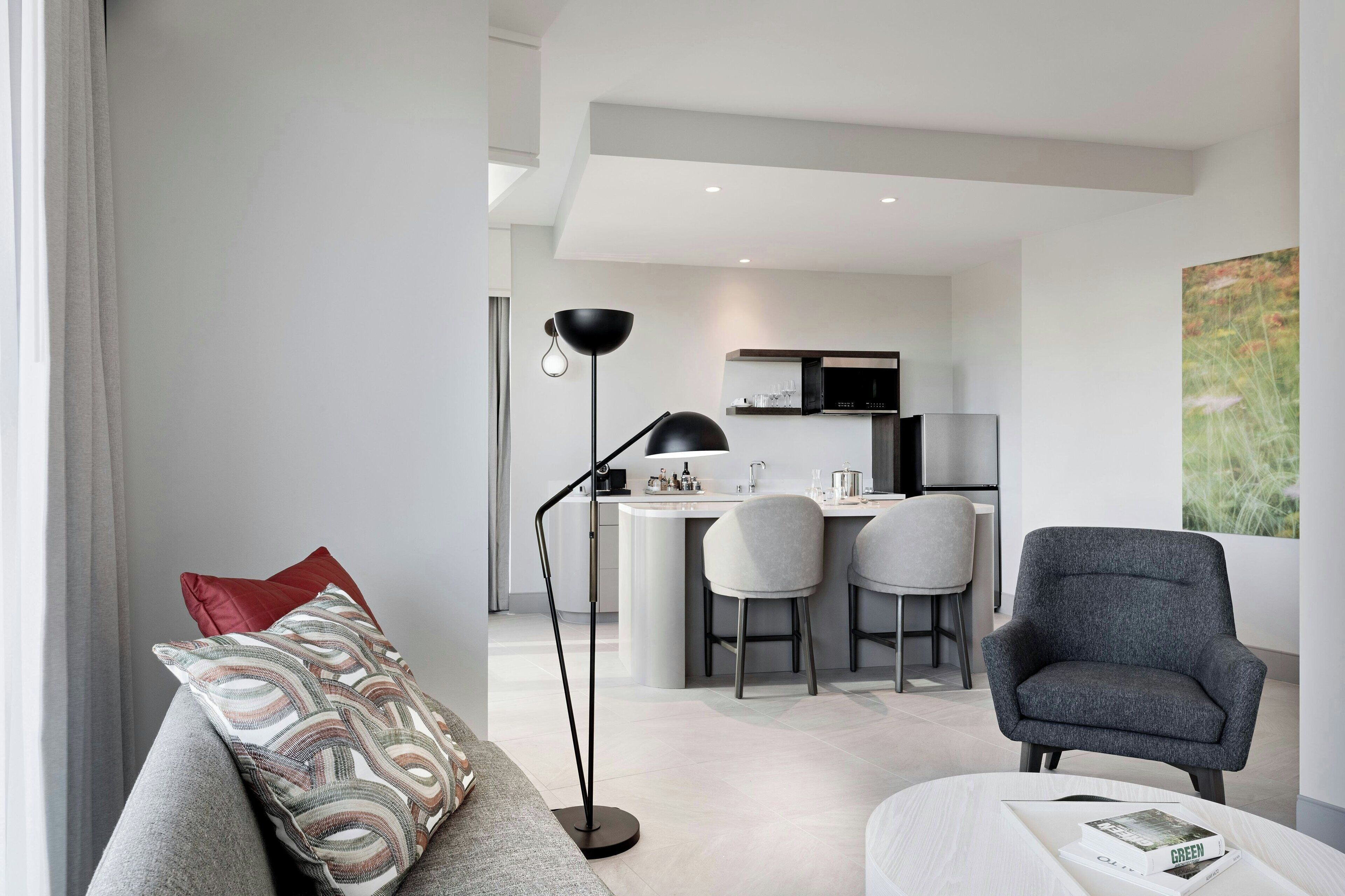 A modern living room with a grey sofa, a floor lamp, and a dining area with a kitchen in the background.