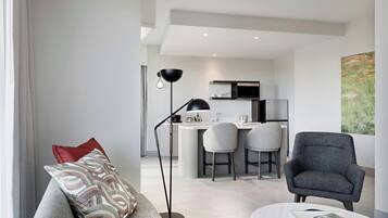 A modern living room with a grey sofa, a floor lamp, and a dining area with a kitchen in the background.