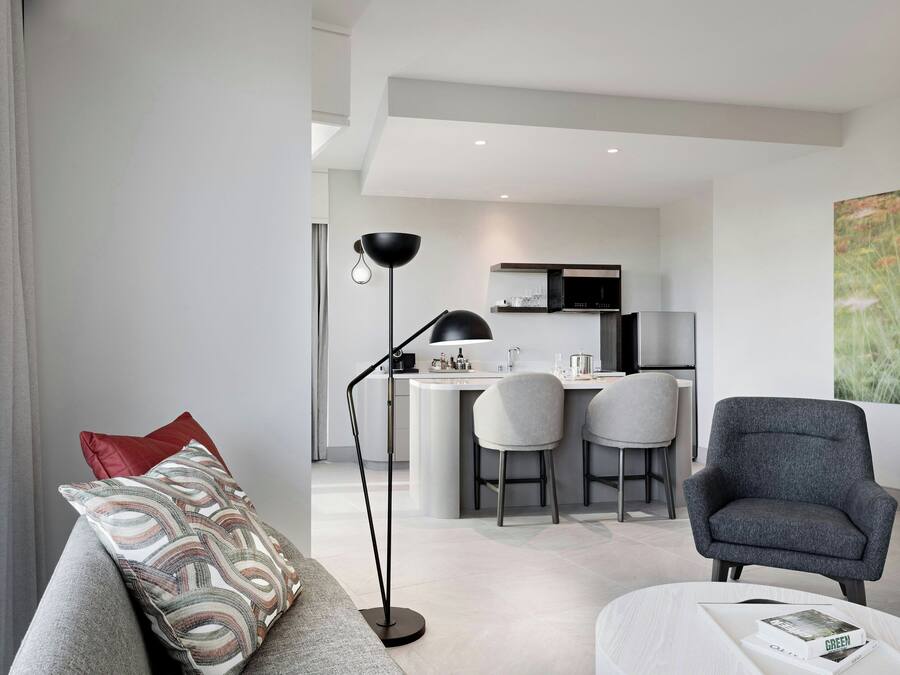 A modern living room with a grey sofa, a floor lamp, and a dining area with a kitchen in the background.