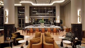 A modern hotel lobby with a central bar, seating arrangements, and a large window providing a view of the interior. - HALL Park Hotel, Autograph Collection (Frisco)