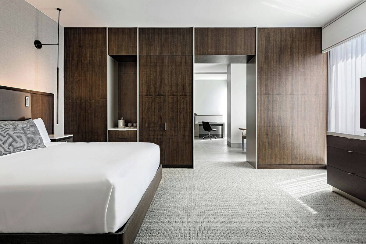 A modern hotel room with a large bed, a desk, and a wardrobe.