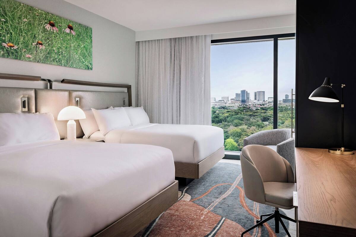 A hotel room with two beds, a desk, and a chair.